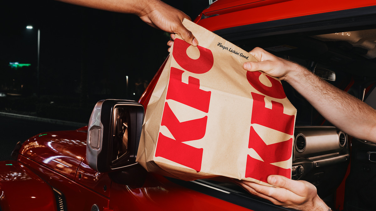 A KFC drive-through handoff at night, featuring the refreshed wordmark and Finger Lickin' Good tagline